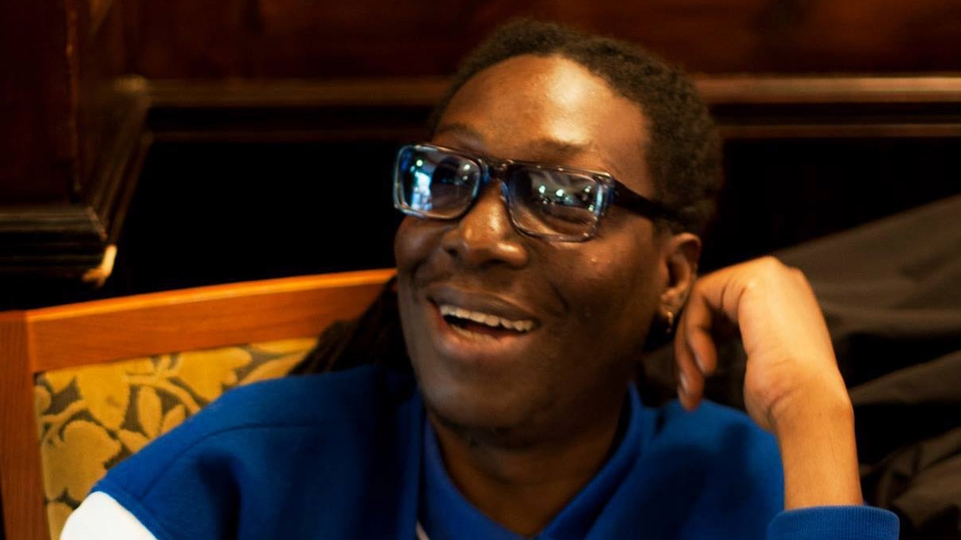 Photo of Leke Adesoye smiling wearing glasses and a blue sweater