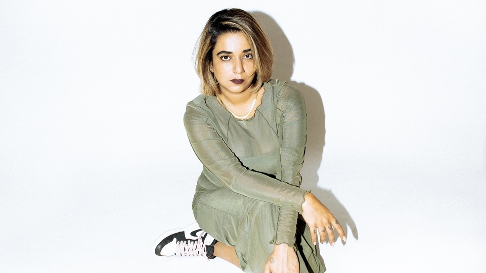 Photo of GoodMostlyBad wearing a green dress and black trainers while sitting on the floor