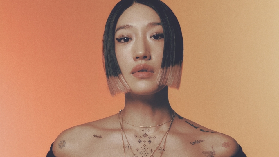 Photo of Peggy Gou with short dip-dyed hair in front of an orange ombre background