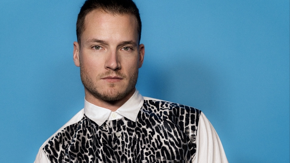 Photo of Mitch Oliver wearing a leopard print shirt in front of a blue background