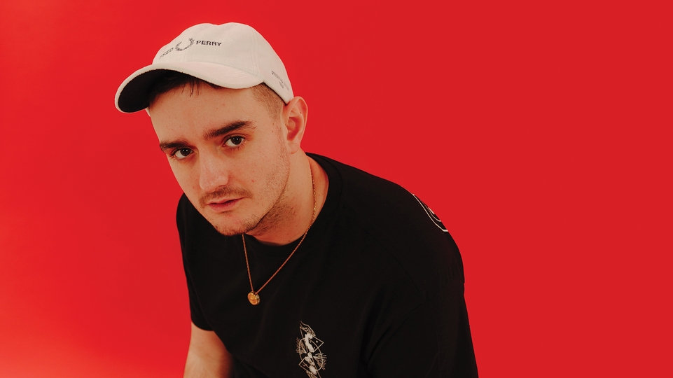 Photo of Ben Hemsley on a red background wearing a black t-shirt and white cap 