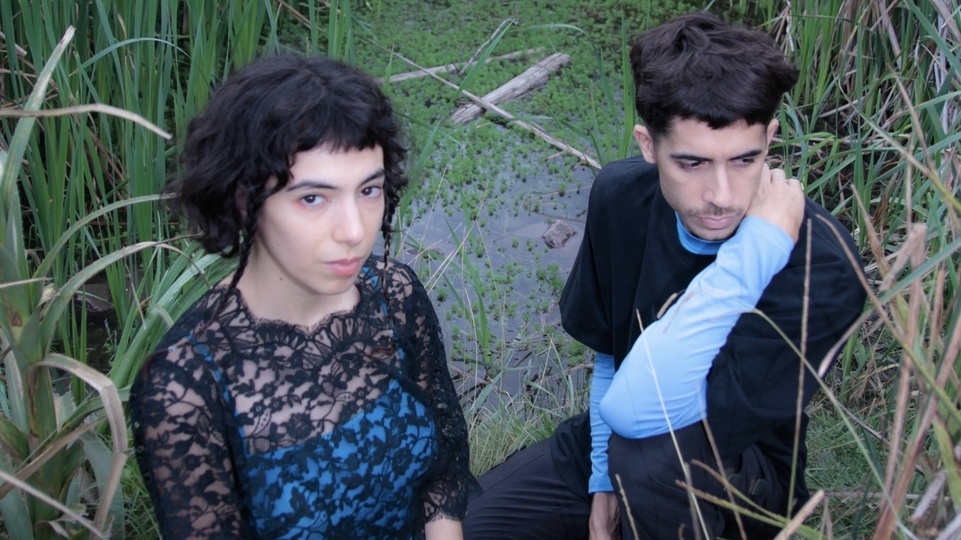 Photo of Lyas posing in dark outfits in front of a green marsh area