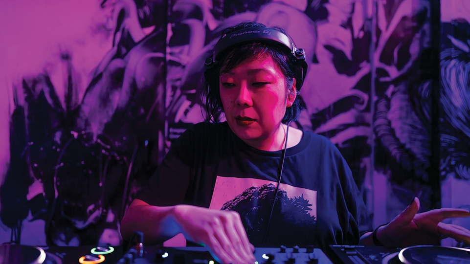Photo of Hiroko Yamamura DJing on CDjs under a pinkish purple light