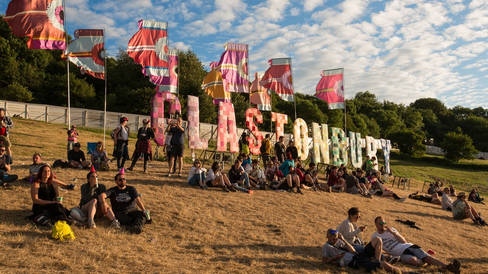 Photo of the colourful Glastonbury sign on a hill against a cloudy blue sky